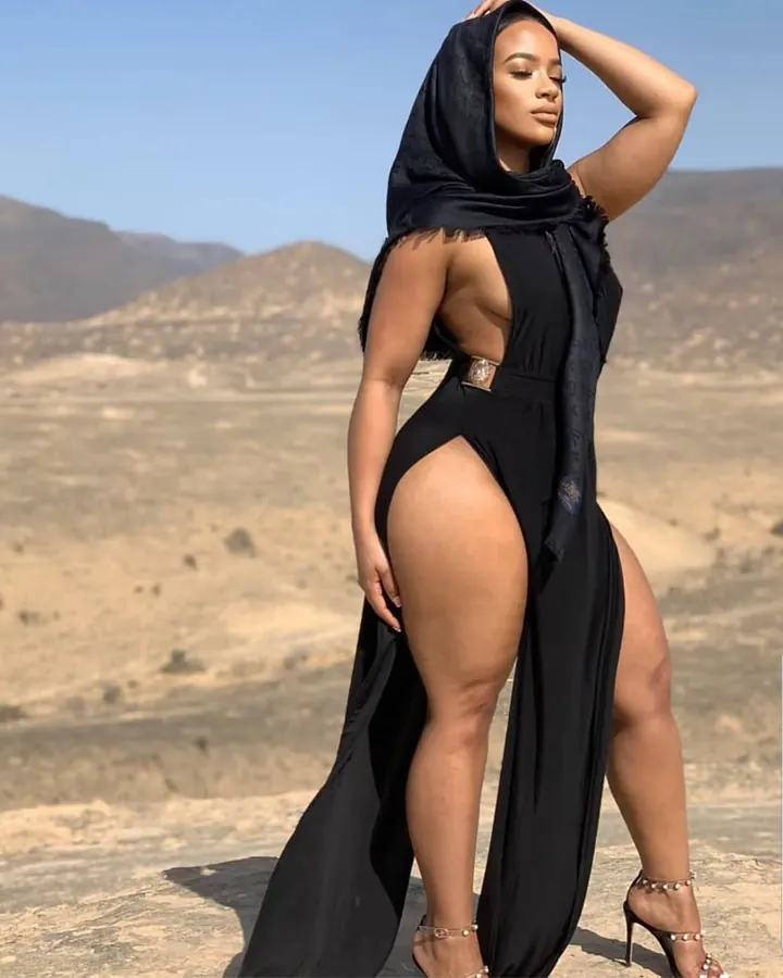 Femme en robe noire avec voile, debout dans un paysage désertique, regardant vers le côté.